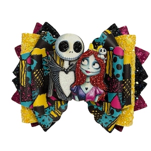 May include: A multi-layered hair bow featuring a patchwork pattern of yellow, blue, pink, and black. The center displays a character with a white skull head and a character with red hair and stitched skin, both accented with black and red glitter.