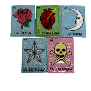 May include: Five colorful embroidered patches with images of a rose, heart with an arrow, crescent moon, star, and skull and crossbones. Each patch has a number and Spanish text, including "La Rosa", "El Corazon", "La Luna", "La Estrella", and "La Calavera".