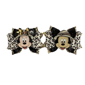 Puede incluir: Dos lazos para el pelo con Mickey y Minnie Mouse. Cada lazo tiene una base negra y dorada con purpurina y una superposición de estampado de leopardo. Mickey y Minnie llevan sombreros de safari. Los lazos están diseñados para niños.