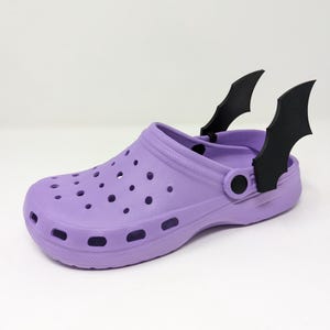 May include: Purple plastic clog with black bat-shaped charms attached to the back strap.