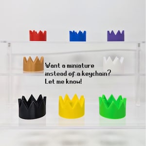 May include: A collection of miniature crown-shaped objects in various colors, including red, blue, purple, gold, white, black, yellow, and green. The text on the image reads, "Want a miniature instead of a keychain? Let me know!"