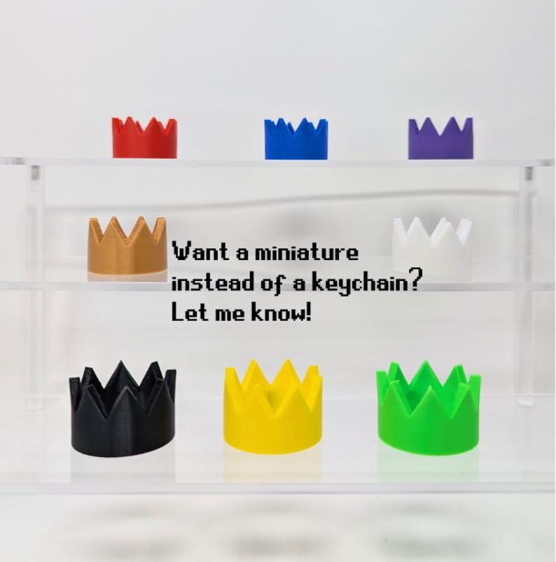 May include: A collection of miniature crown-shaped objects in various colors, including red, blue, purple, gold, white, black, yellow, and green. The text on the image reads, "Want a miniature instead of a keychain? Let me know!"
