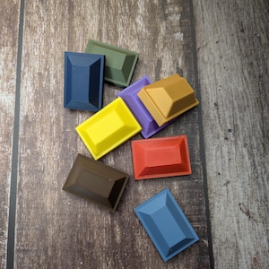 Puede incluir: Una colección de objetos rectangulares multicolores con bordes biselados. Los objetos son en tonos de azul, verde, amarillo, morado, marrón y rojo. Están dispuestos sobre una superficie de madera.