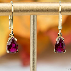 May include: A pair of gold dangle earrings with teardrop-shaped red gemstones.
