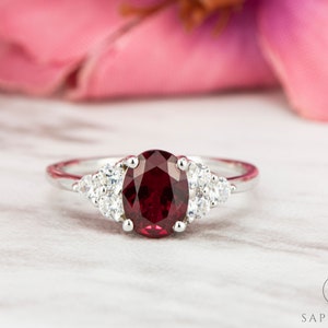 May include: A silver ring featuring a large oval ruby gemstone, surrounded by smaller white gemstones.