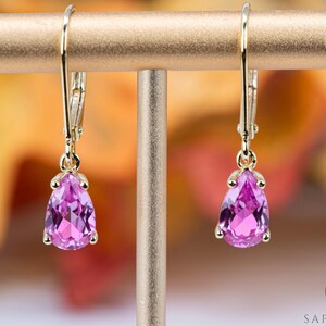 Può includere: Un paio di orecchini d'oro con pietre preziose rosa a forma di pera.