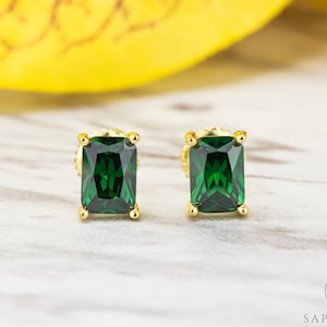 May include: A pair of gold earrings with emerald green square-shaped gemstones.