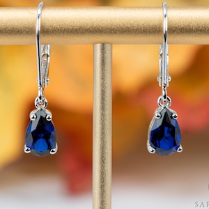 May include: A pair of silver dangle earrings with teardrop-shaped blue gemstones.