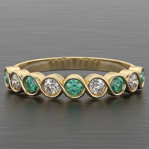 May include: A gold ring with alternating emerald and diamond gemstones. The ring's design features a repeating pattern of gemstones. The ring is displayed on a grey surface.
