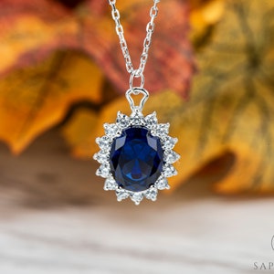 May include: A silver necklace with a large blue oval gemstone surrounded by smaller clear gemstones. The pendant is in a halo setting.