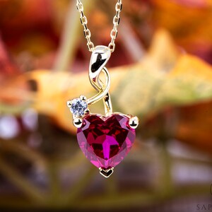 Peut inclure: Un collier en or avec un pendentif en forme de cœur en rubis et un petit accent en diamant. Le pendentif est en forme de cœur avec un motif en spirale.