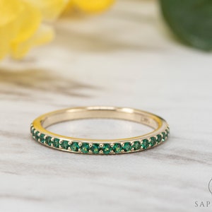 May include: A thin gold band with a row of small, green gemstones.