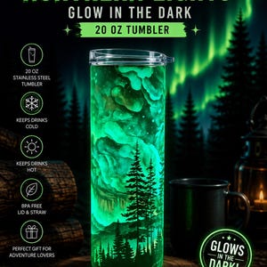 May include: A 20 oz stainless steel tumbler featuring a glow-in-the-dark design of a forest landscape under the northern lights. The text reads NORTHERN LIGHTS, GLOW IN THE DARK, 20 OZ TUMBLER, and GLOWS IN THE DARK. It includes a clear lid.