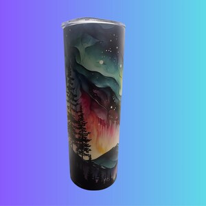 May include: A stainless steel tumbler with a clear lid. The tumbler has a watercolour design of a night sky with the aurora borealis, mountains, and trees. The colours include shades of blue, green, red, and black.