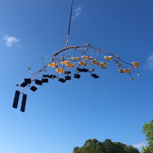 May include: A copper wire mobile with black and yellow geometric shapes hanging from a copper wire frame against a blue sky.