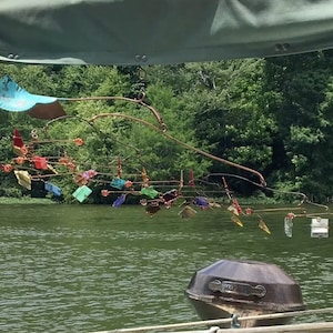 Może przedstawiać: Kolorowy mobil wykonany z metalu i szkła wisi nad zbiornikiem wodnym. Mobil charakteryzuje się różnorodnością kształtów i kolorów, w tym niebieskim, zielonym, czerwonym, żółtym i pomarańczowym. Mobil jest zawieszony na drucie i delikatnie kołysze się na wietrze.