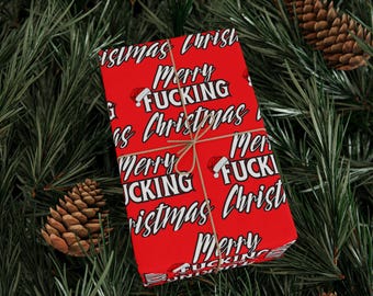 May include: Red Christmas wrapping paper with the text "Merry Fucking Christmas" in white. The paper is tied with twine and surrounded by pine needles and pine cones.