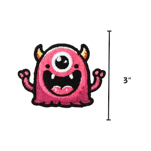 May include: Pink monster with one eye, horns, and a big smile. The monster is 3 inches tall.