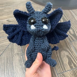 May include: A crocheted blue gargoyle with large black eyes and white teeth. The gargoyle has wings and a tail.