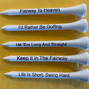 May include: Five white golf tees with black lettering. The text on the tees reads: "Fairway To Heaven", "I'd Rather Be Golfing", "Hit 'Em Long And Straight", "Keep It In The Fairway", and "Life Is Short, Swing Hard".