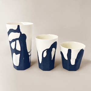 May include: Three white ceramic cups with a blue abstract design. The cups are different sizes and are arranged in a row from largest to smallest.