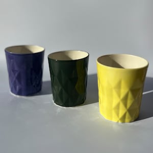 May include: Three ceramic cups with a geometric pattern. The cups are purple, green, and yellow.