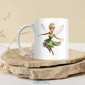 May include: White ceramic mug with a colorful illustration of Tinkerbell, a fairy with green wings and a green dress, flying.