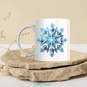 Op de afbeelding: Witte keramische mok met een blauw en wit sneeuwvlokontwerp. De sneeuwvlok is gedetailleerd en ingewikkeld.