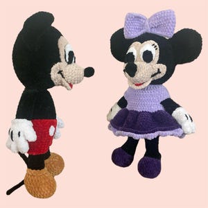 May include: A crocheted Mickey Mouse and Minnie Mouse plush toy set. Mickey is wearing red shorts and black shoes. Minnie is wearing a purple dress and shoes. Both have black eyes and white gloves.