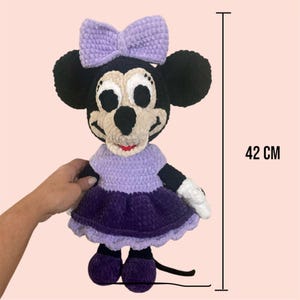 May include: A crocheted plush toy of a purple-dressed Mickey Mouse character, standing 42 cm tall. The toy has a purple dress with a white bow, black ears, and a black tail.
