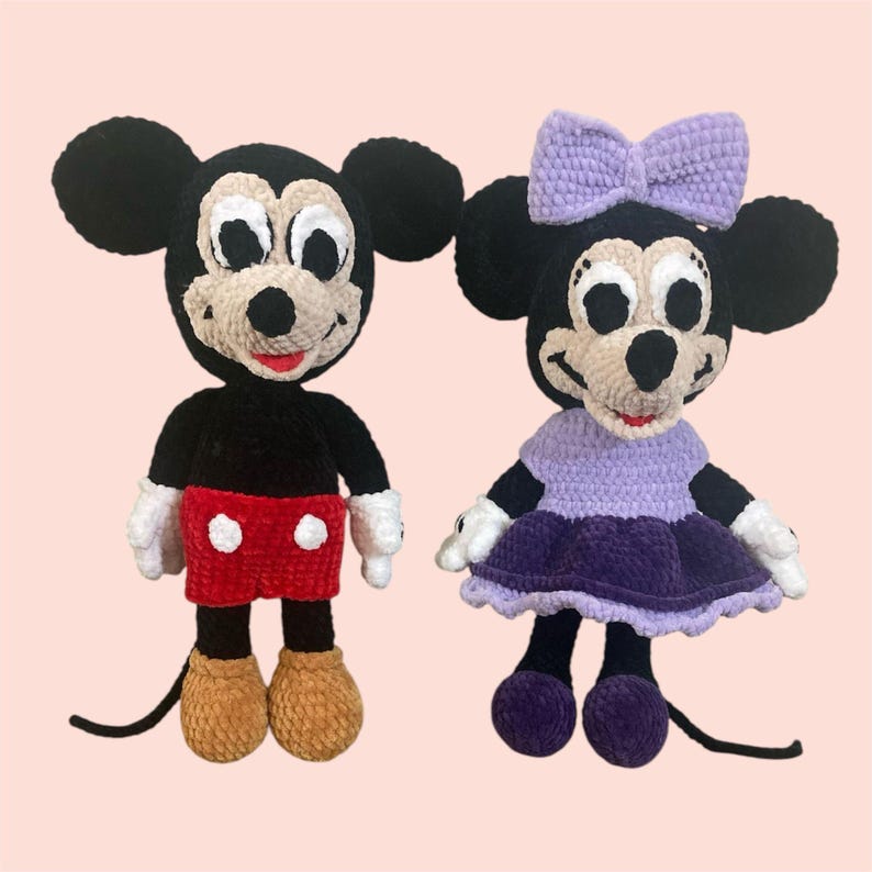 May include: A pair of crocheted Mickey Mouse and Minnie Mouse plush toys. Mickey is wearing red shorts and brown shoes. Minnie is wearing a purple dress and purple shoes. Both have black eyes and white accents.