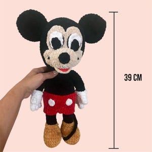 May include: A crocheted Mickey Mouse plush toy with black fur, white gloves, red shorts, and brown shoes. The toy is 39 cm tall.
