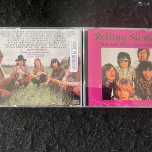 Puede incluir: Un CD de los Rolling Stones, "Mad Shadows", en una caja transparente. La portada es rosa con una foto de la banda. La parte trasera muestra una foto de la banda y una lista de canciones. Hecho en Alemania.