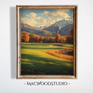 May include: A framed landscape painting of a golf course with a mountain backdrop. The artwork features a green golf course, a small pond, and trees with autumn foliage. The sky is blue with fluffy white clouds. The frame is a light brown color. The text "- MACWOODSTUDIO -" is at the bottom.