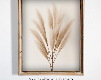 Op de afbeelding: Een ingelijste print met beige pampasgras op een crèmekleurige achtergrond, geplaatst in een lichtbruine houten lijst. Het kunstwerk heeft de tekst "- MACWOODSTUDIO -" onderaan. De lijst voegt een rustieke toets toe aan het botanische thema.