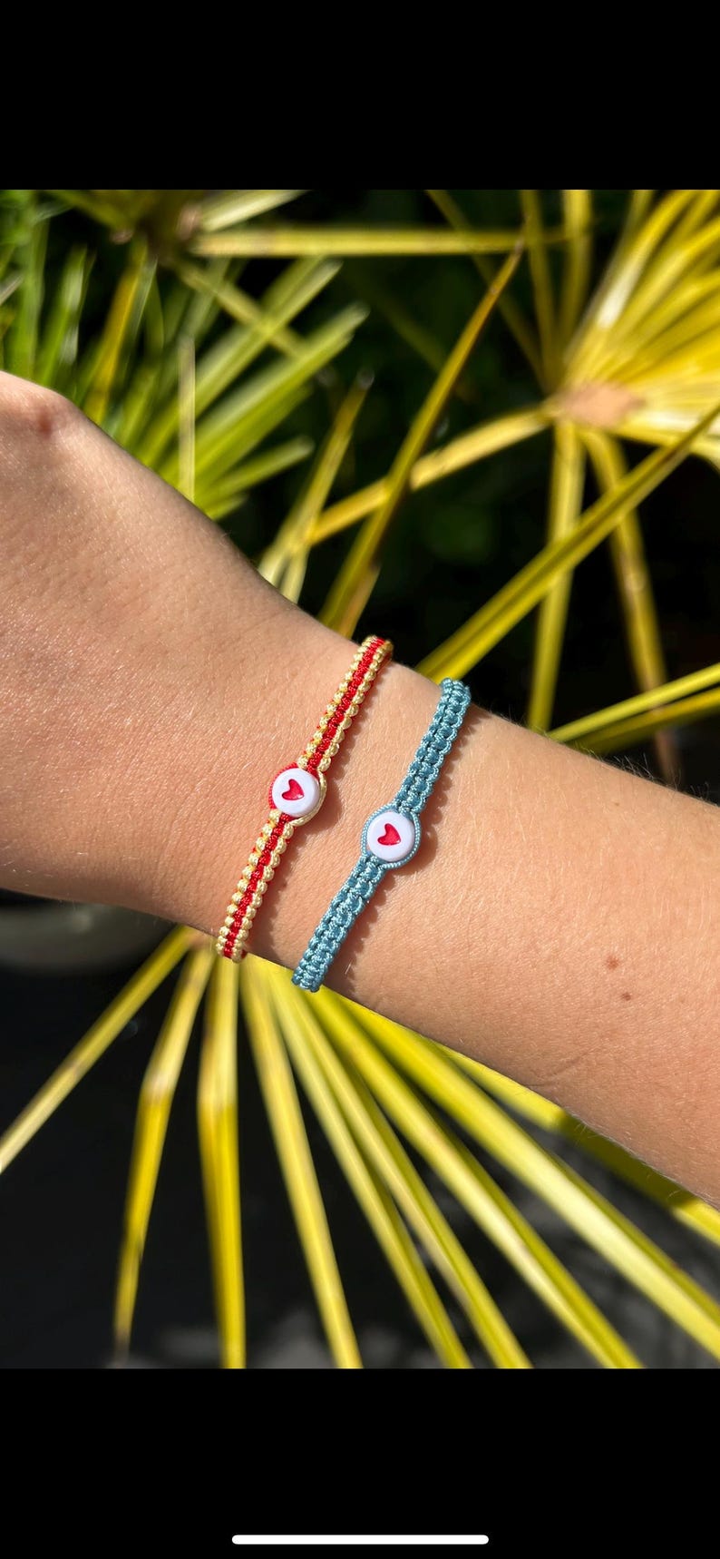 May include: Two friendship bracelets with heart-shaped buttons. One bracelet is red and yellow, the other is blue.