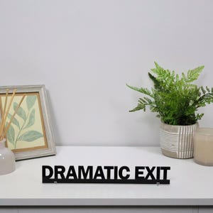 DRAMATIC EXIT black acrylic sign displayed on a shelf with home decor, popular with drama lovers, theatre enthusiasts and stylish bedrooms.