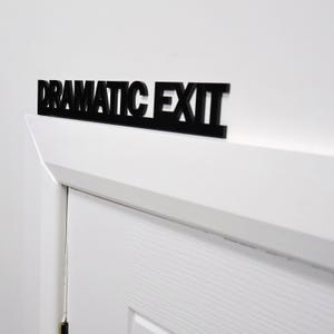 Close-up of DRAMATIC EXIT door topper above a white door frame.