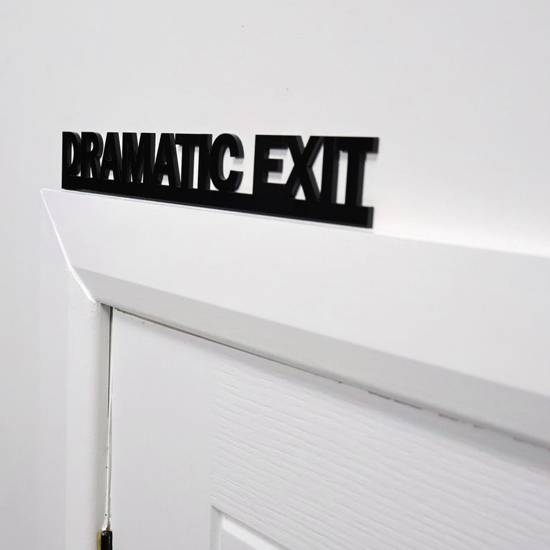 Close-up of DRAMATIC EXIT door topper above a white door frame.