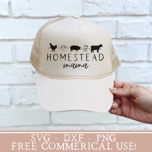 Op de afbeelding: Een beige trucker-pet met een zwart-wit ontwerp met de tekst "Homestead mama" met een kip, een brood, een varken, een pot en een koe.  SVG-, DXF- en PNG-bestanden zijn beschikbaar voor gratis commercieel gebruik.