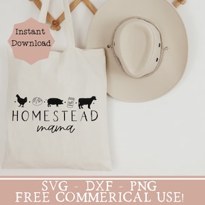 Op de afbeelding: Een witte tote bag met de tekst "Homestead mama" en een rij van boerderij-gerelateerde pictogrammen: een kip, een brood, een varken, een pot melk en een koe. De tas hangt aan een houten rek met een beige cowboyhoed ernaast. De tekst "SVG - DXF - PNG FREE COMMERCIAL USE!" staat onderaan de afbeelding.