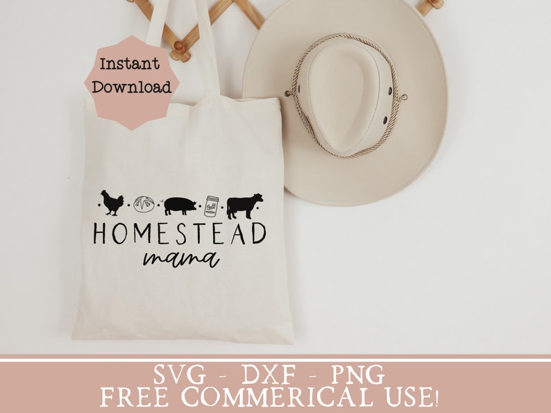 Op de afbeelding: Een witte tote bag met de tekst "Homestead mama" en een rij van boerderij-gerelateerde pictogrammen: een kip, een brood, een varken, een pot melk en een koe. De tas hangt aan een houten rek met een beige cowboyhoed ernaast. De tekst "SVG - DXF - PNG FREE COMMERCIAL USE!" staat onderaan de afbeelding.