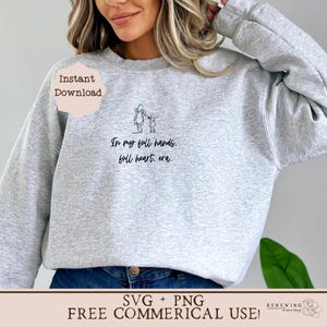 K&ouml;nnte beinhalten: Ein graues Sweatshirt mit einer schwarzen Linienzeichnung einer Mutter und eines Kindes, die Hand in Hand gehen. Der Text "In my full hands, full heart, era." ist unter der Zeichnung gedruckt.