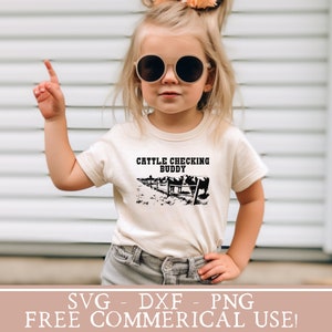 以下が含まれることがあります： 白いTシャツを着た小さな子供が、「Cattle Checking Buddy」という文字と、フェンスの後ろに牛の黒いシルエットが描かれています。子供は丸いサングラスをかけており、右手を指差しています。背景は白い木製の羽目板の壁です。
