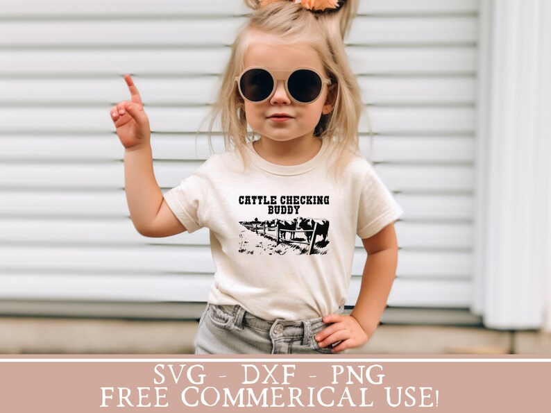 以下が含まれることがあります： 白いTシャツを着た小さな子供が、「Cattle Checking Buddy」という文字と、フェンスの後ろに牛の黒いシルエットが描かれています。子供は丸いサングラスをかけており、右手を指差しています。背景は白い木製の羽目板の壁です。