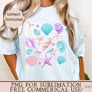 May include: A light blue t-shirt with a design of pastel pink, blue, and purple seashells, starfish, and bows. The design is centered on the shirt.