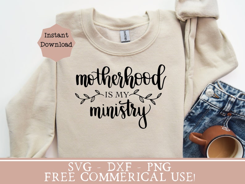 Pu&ograve; includere: Una felpa beige con il testo "Motherhood is my ministry" in lettere corsive nere. Il testo &egrave; circondato da due piccoli rametti di foglie. La felpa &egrave; appoggiata su una superficie bianca con un paio di jeans e una tazza da caff&egrave;.