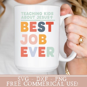 May include: White ceramic mug with the text "TEACHING KIDS ABOUT JESUS+ BEST JOB EVER" in colorful letters. The mug is being held by a person's hand. The text "SVG - DXF - PNG FREE COMMERICAL USE!" is at the bottom of the image.
