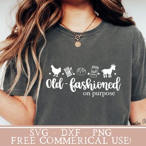 May include: A gray t-shirt with a white graphic design that says "Old-fashioned on purpose". The graphic includes a chicken, spool of thread, a loaf of bread, a jar of jam, and a goat.