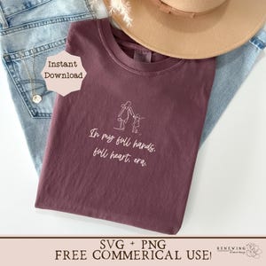K&ouml;nnte beinhalten: Ein maroonfarbenes T-Shirt mit einer wei&szlig;en Umrandung einer Mutter und eines Kindes, die gehen, und dem Text "In my full hands, full heart, era."